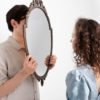 Man standing behind a mirror while a woman stands in front of it