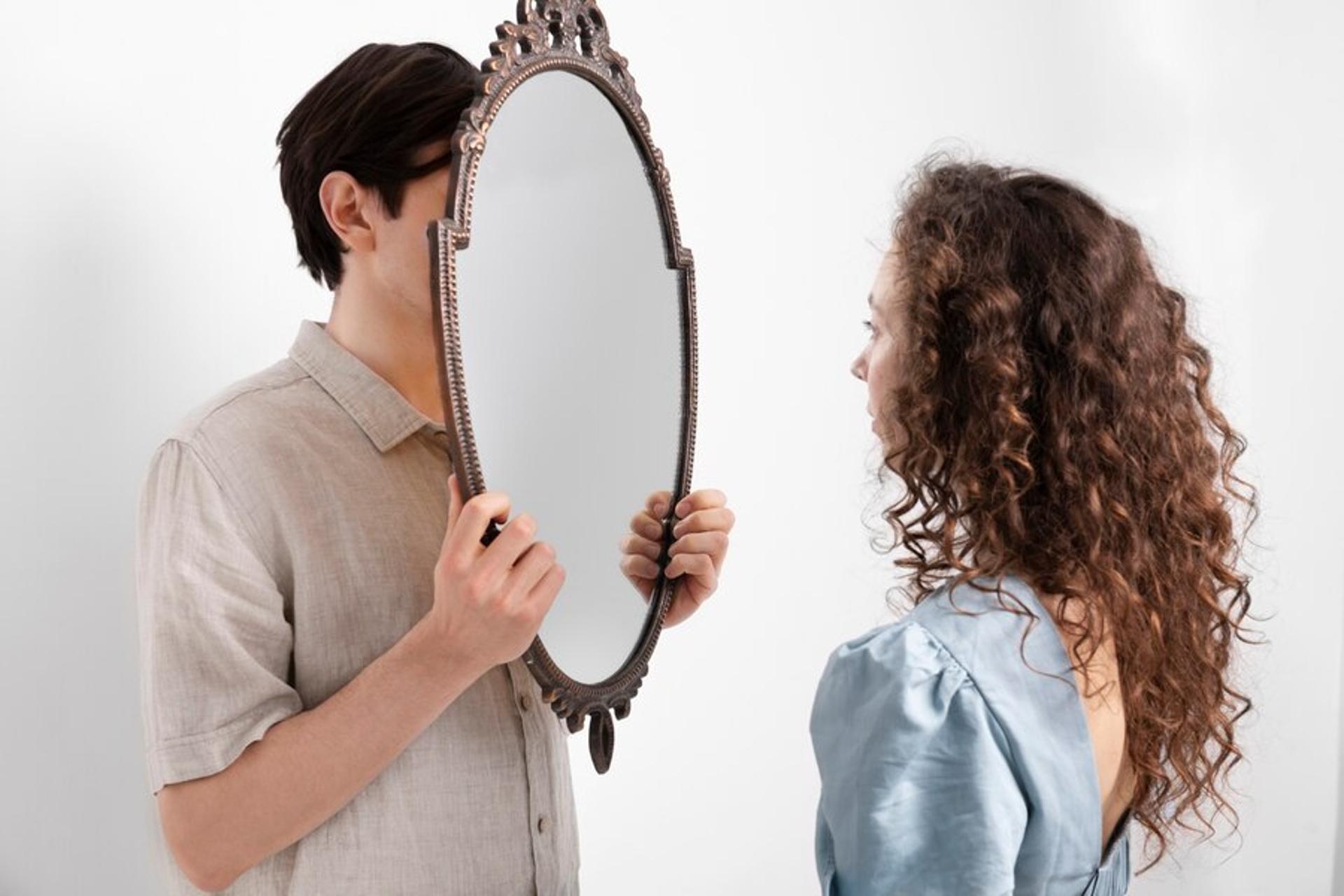 Man standing behind a mirror while a woman stands in front of it